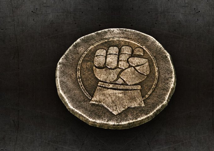 A weathered gold coin emblem featuring a raised clenched fist inside a circular border rests on a scratched dark surface, visually echoing the post's themes of strength, unity, and solidarity within the Iron Allies community.