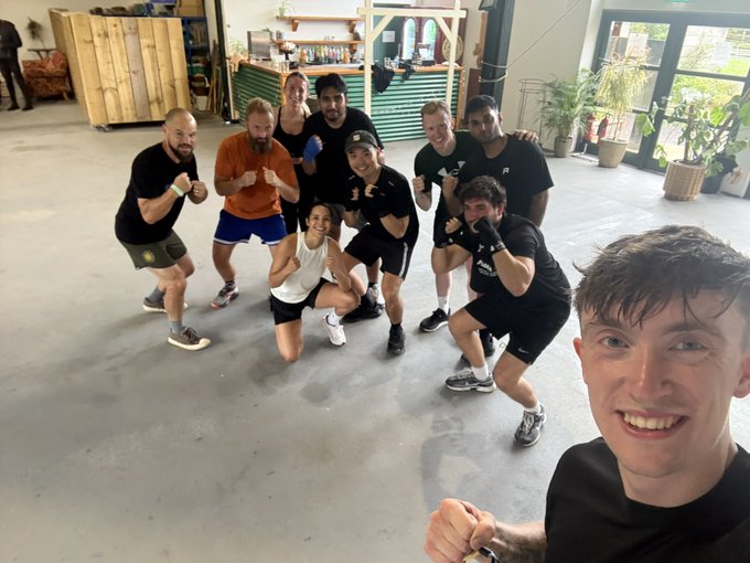 A group of smiling people pose in boxing stances with gloved fists raised at a gym, with one young man taking the selfie in the foreground. The image captures the CastleDAO boxing club session mentioned in the post, showing participants in athletic gear inside what appears to be a casual workout space.