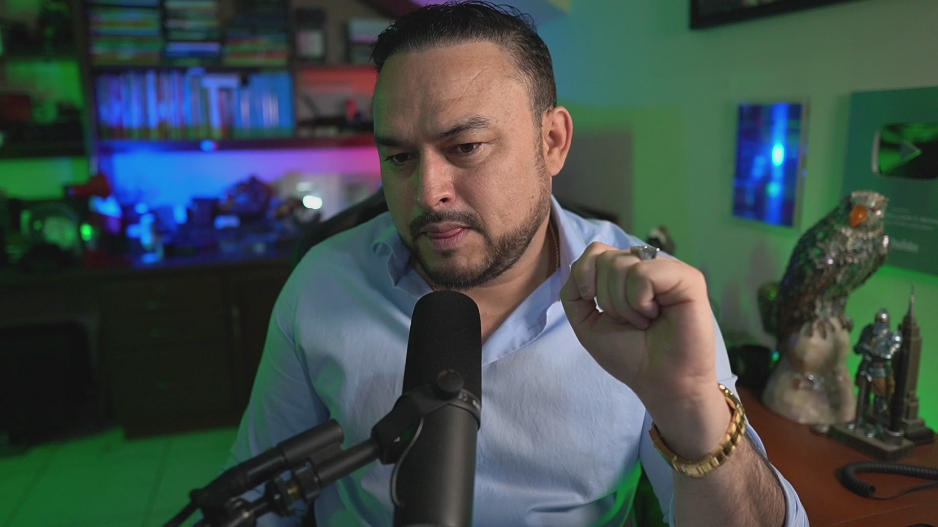 The image shows a man sitting at a desk with a microphone, likely preparing for or just finished recording a podcast. The background features a green wall adorned with various objects such as books and a TV screen. There are also two birds visible in the scene, one on top of another object. The post that accompanies this image is titled "Bitcoin en Soporte Importante: Lo Que Nadie Te Está Contando". This suggests that the man might be discussing or reviewing Bitcoin, which is an important topic for many people to understand and stay informed about.
