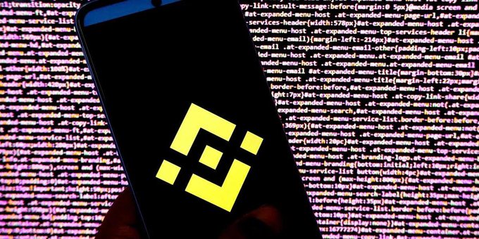 A smartphone displays the yellow Binance logo against a backdrop of colorful code, visually reinforcing the article about the cryptocurrency exchange's internal security measures, where its red team conducts monthly mock phishing attacks on employees to combat hackers.