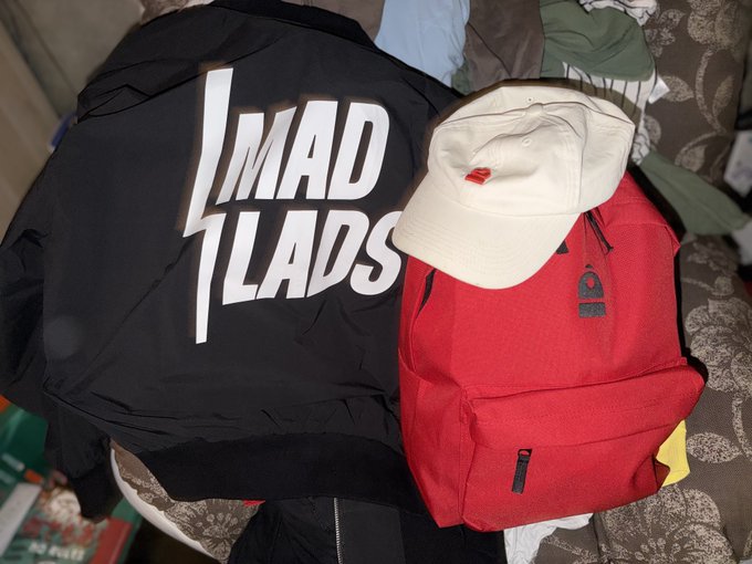A pile of merchandise including a black "MAD LADS" t-shirt, a red backpack, and a white baseball cap, prepared for tomorrow's Solana Summit at Sava Centar as mentioned in the post.