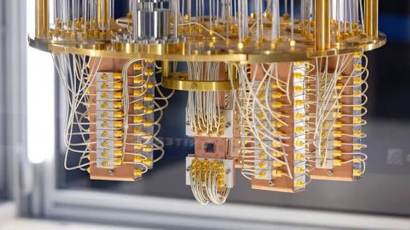 A quantum computing dilution refrigerator with cascading gold and copper stages housing intricate wiring and components, featuring the "IBM Quantum" and "STFC" logos visible on the display case. The image illustrates the specialized, complex hardware that QuipNetwork aims to democratize by extending access beyond well-funded institutions to everyday developers.