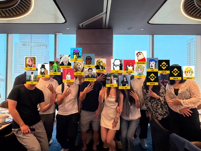 A group of people pose together indoors with cartoon avatars and labels covering their faces, with Chinese text on the labels.