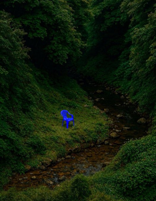 A lone blue plastic chair sits abandoned in a lush green forest beside a shallow rocky stream, embodying a quiet Sunday escape into nature.
