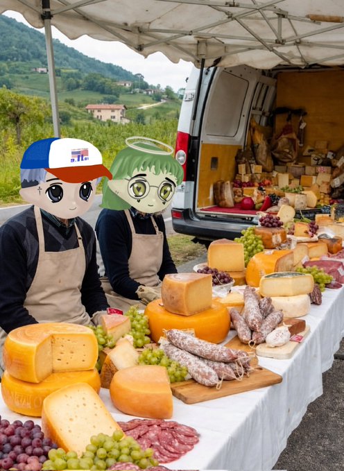 Two anime-style characters with chibi proportions wearing aprons standing behind a table displaying an abundant spread of cheeses, meats, and grapes at an outdoor market.