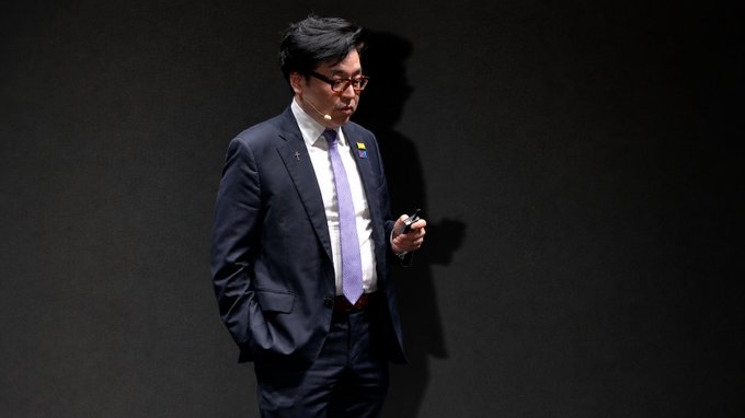 The image features a man dressed in a suit, standing against a black background with his hands in his pockets. He appears to be looking down at something or someone, possibly a cell phone. The caption of the image reads "BIG: Tom Lee says Bitmine's Ethereum treasury generates $1M per day in staking rewards." This suggests that the man might be discussing or reviewing some information related to the Ethereum blockchain and its potential for generating financial returns through staking.