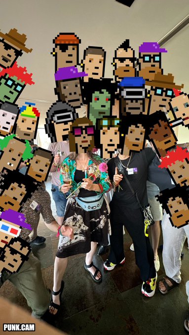 A group of people pose together for a group photo, with their faces replaced by pixelated Cryptopunk NFT character heads in various colorful designs, embodying the post's theme of Cryptopunks taking over the timeline. The watermark "PUNK.CAM" appears in the bottom left corner, reinforcing the NFT-focused aesthetic.