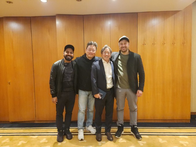 Four men posing together for a photo, smiling at the camera in a wood-paneled room.