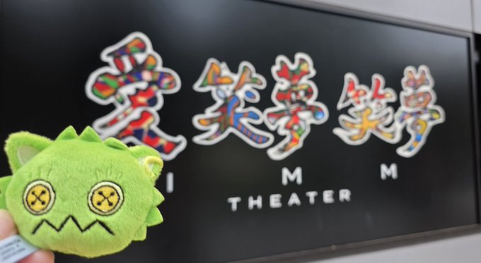The image features a green stuffed animal, possibly a toy or plush, standing next to a blackboard with Chinese characters written on it. The text "I M Theater" can be seen below the blackboard. This suggests that there might be an event related to theater in progress at this location, as indicated by the presence of the Chinese characters and the context provided by the post.