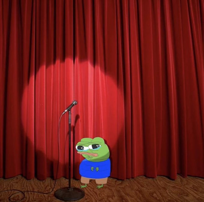 A cartoon frog character with sad eyes wearing a blue shirt and headphones stands on a wooden stage in front of a red curtain with a spotlight, next to a microphone on a stand.