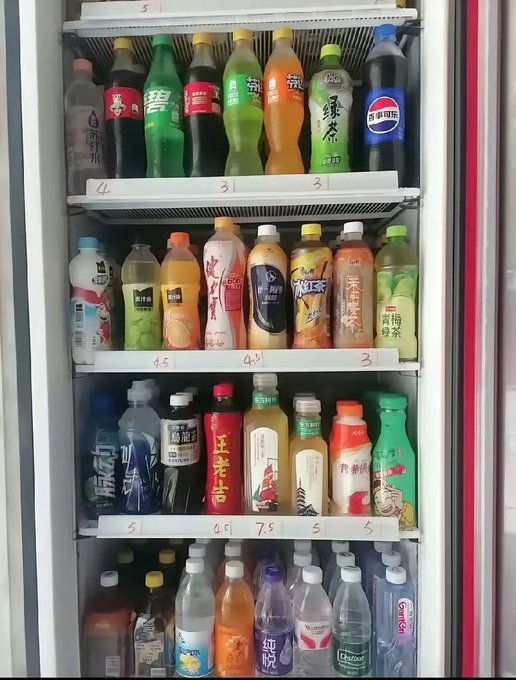 A refrigerator stocked with various bottled beverages including sodas, juices, and teas, with handwritten price labels on the shelves like '4', '3', '4.5', '7.5', and '5'.