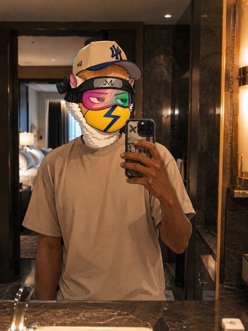 A mirror selfie of a person wearing a colorful mask, an 'LA' baseball cap, and a beige t-shirt, holding a phone with a decorated case in a hotel bathroom.