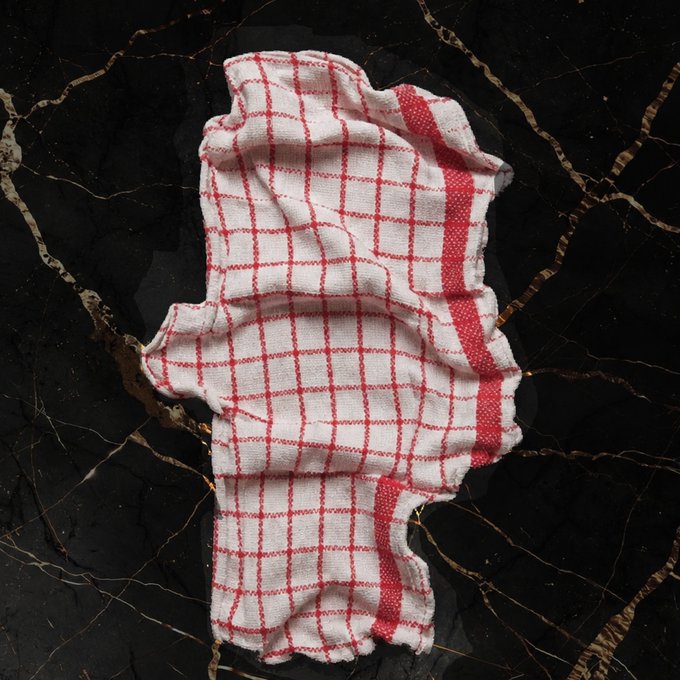A crumpled white kitchen towel with a red windowpane check pattern rests on a black marble surface with gold veining.