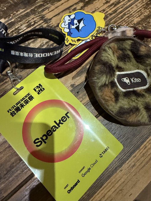 A conference badge labeled 'Speaker' for the FUTUREMODE FM 26 event, lying next to a leopard-print Kite branded pouch and a lanyard featuring the event's blue mascot logo.