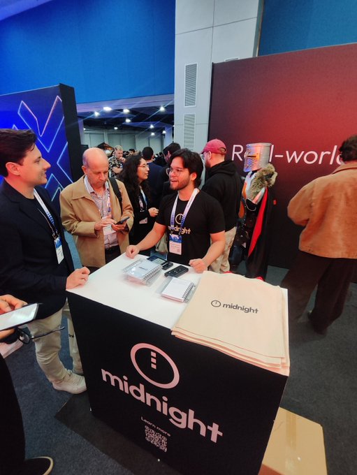 An exhibition booth for 'midnight' where attendees are gathered around a counter with branded tote bags and informational materials.