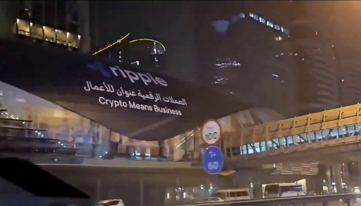 The image shows a city street at night with buildings and cars passing by, including a large billboard featuring a cartoon character that says "ripple" along with the words "Crypto Mea Business". The text also mentions the expansion of digital assets in the Middle East region and the future of blockchain adoption.