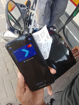 A close-up shot of a hand holding a black Samsung smartphone displaying a digital wallet card with the 'y' logo for CBE Birr, with a payment terminal and a printed receipt visible in the background.