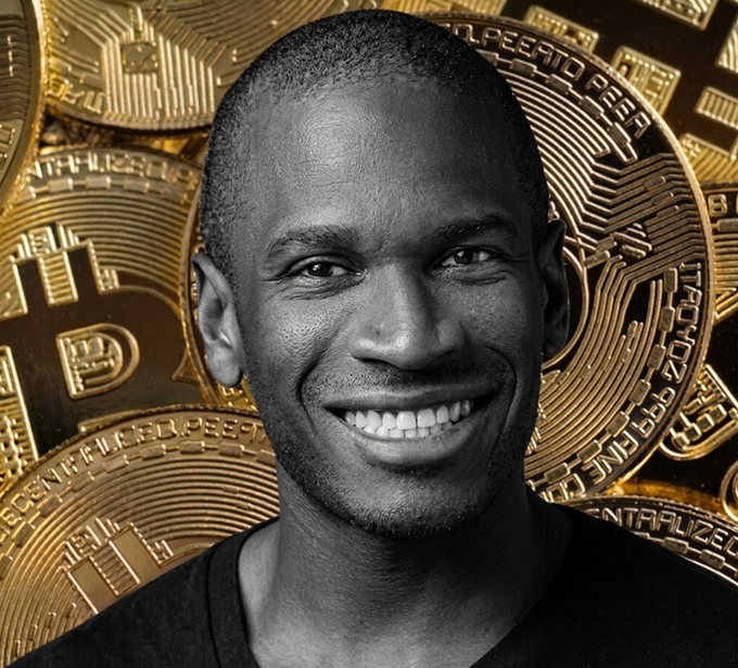The image features a man with a big smile, wearing a black shirt, standing against a background of gold coins. The coins are scattered around him, creating an interesting visual effect that highlights his presence. The caption above the photo reads "Tại sao Arthur Hayes bán toàn bộ hyân nhạy trend và thị trường, anh ta nói rằng có thấp hơn mua lại ở vị thế thấp hơn mua lại khôn ngoan." The man's smile and the surrounding coins create a sense of abundance, wealth, or prosperity.
