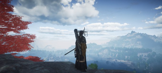 A samurai character in dark robes with a wide-brimmed hat and katana stands on a cliff overlooking a vast mountain landscape with red maple leaves, likely from the video game Ghost of Tsushima.