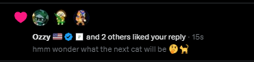 A social media notification shows that "Ozzy 🇺🇸 ✅ and 2 others liked your reply" posted 15 seconds ago, with the reply text reading "hmm wonder what the next cat will be 🐱🐕" This playful reply about guessing upcoming cat announcements relates to the post praising a user (@MEADGod) as "a man of culture who appreciates thinking."