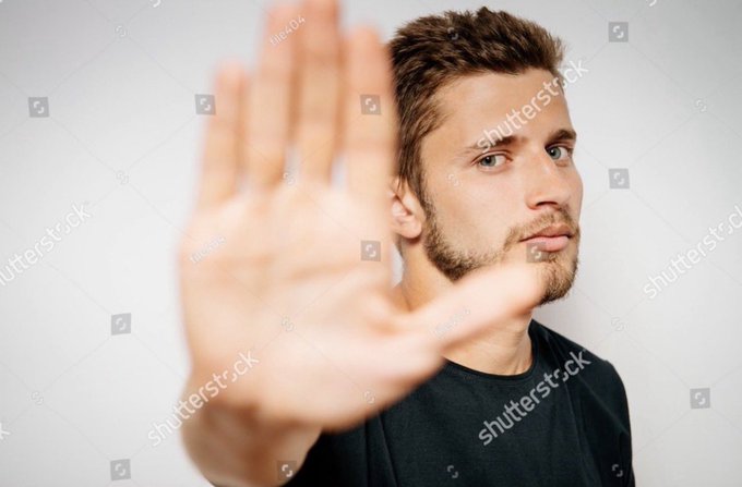 A young man with a beard holding his hand up in a stop gesture, photographed against a plain light background with Shutterstock watermarks.