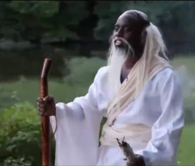 An elderly bearded man in white robes holds a wooden staff while gazing serenely into the distance, embodying the calm wisdom of someone above market fluctuations. His tranquil expression pairs perfectly with the joke's punchline, suggesting an enlightened perspective on crypto's volatility—that downturns are simply a setup for the inevitable rebound.