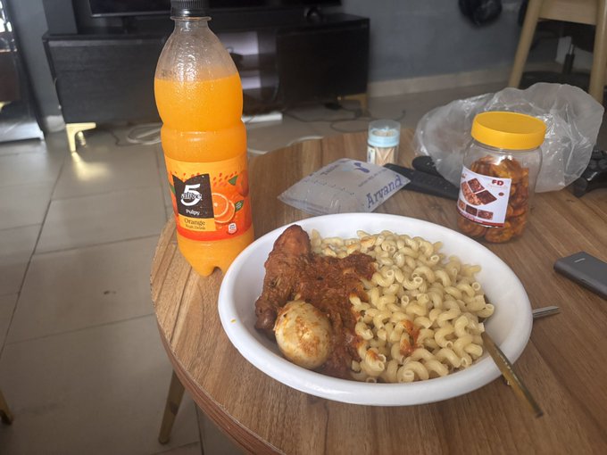 A bottle of "5 Alive" orange juice, a jar labeled "FD," and an "Arwana" rice packet sit beside a bowl of elbow macaroni, fried egg, and stewed meat on a wooden table—capturing the post's playful nod to hearty, home-style eating as a web3 lifestyle.