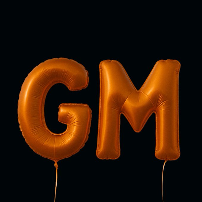 Two metallic orange foil balloons shaped as the letters 'G' and 'M' float against a black background.