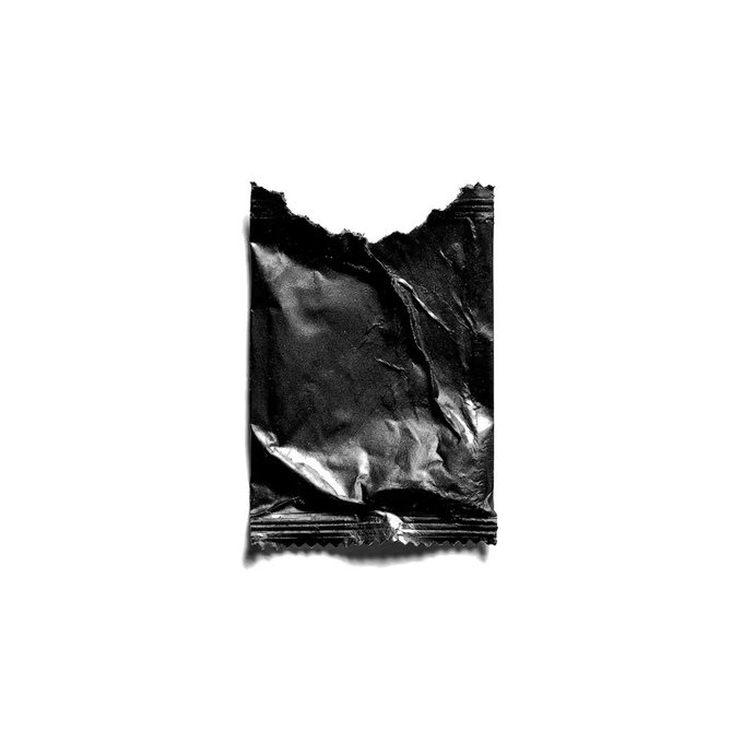 A black and white photograph of a torn, opened candy or snack wrapper, possibly chocolate, against a white background.