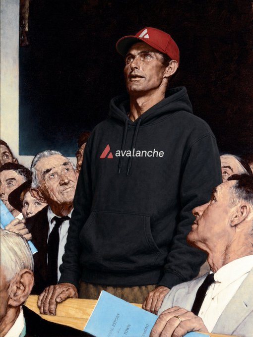 The image features a man wearing a black hoodie with an Avalanche logo, standing next to a group of people who are also wearing black hoodies. The man in the foreground has his hands on his hips, while others around him look at him attentively or engage in conversation. There is a book placed near one of them and another person holding a blue folder close by. The scene suggests that they might be attending an event related to avalanche safety or discussing business matters involving the ski resort industry.