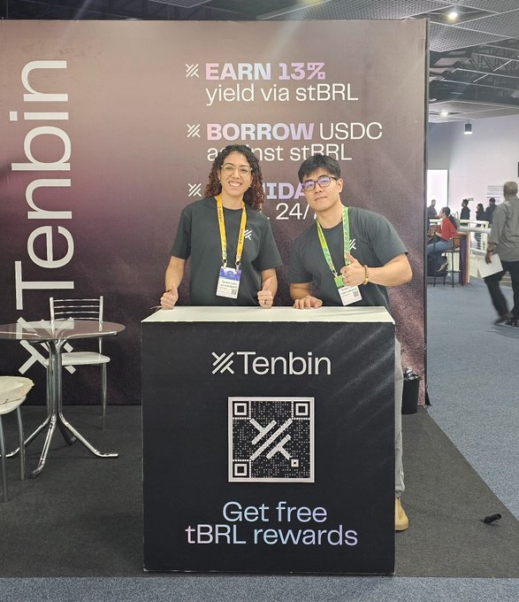 Two representatives from Tenbin pose behind their promotional booth at Blockchain Rio, standing next to a large QR code display advertising "Get free tBRL rewards." The banner behind them promotes their key services: "EARN 13% yield via stBRL," "BORROW USDC against stBRL," and a 24/7 offering, capturing the team's appreciation for community feedback at the event.