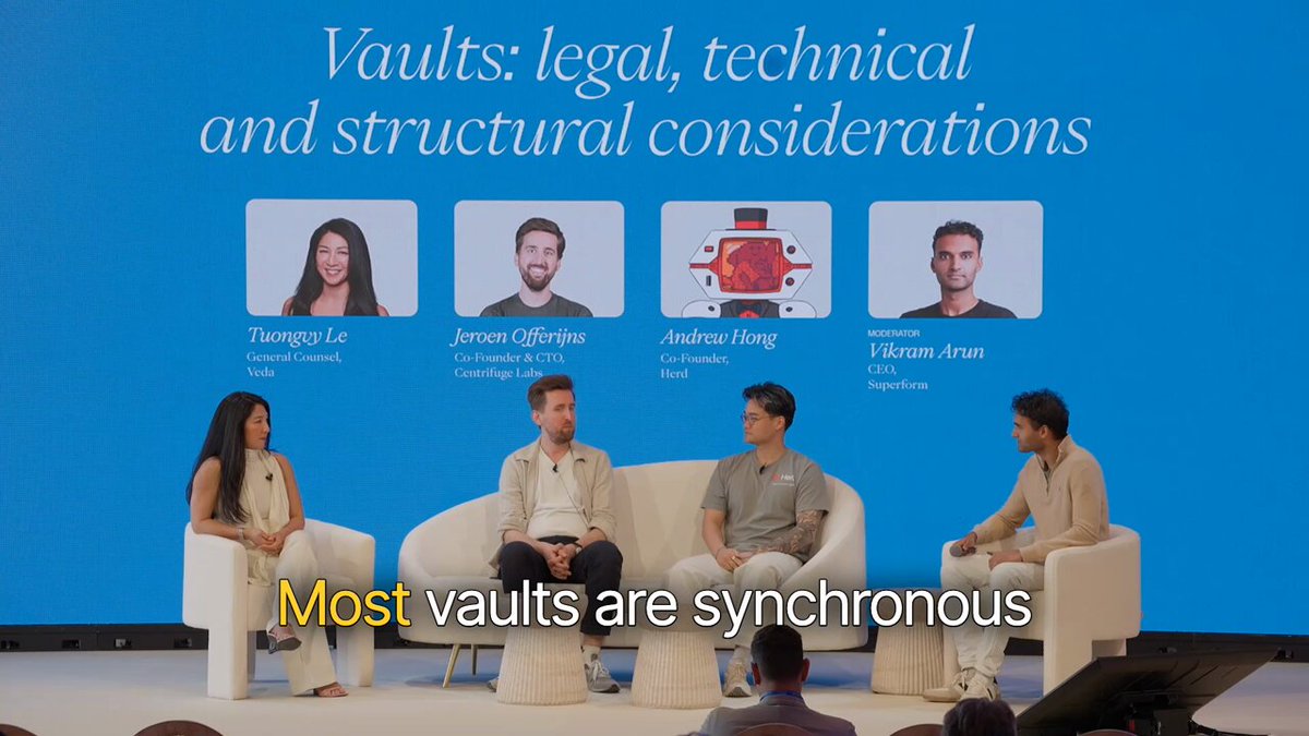 The image shows a group of people sitting around a table with white couches arranged for them. The scene appears to be set up for an event or discussion where they are talking about synchronous operations and their implications, possibly related to asset management.