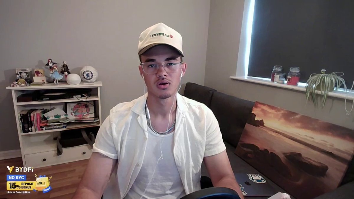 The image shows a man sitting in front of a computer screen while wearing glasses and a white shirt. The background features a window with blinds that allows natural light into the room, creating an atmosphere for work or leisure activities. A clock can be seen on the wall next to the window.