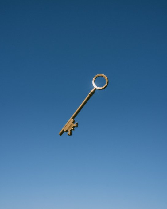 A golden key floats against a clear blue sky, glinting in the sunlight.
