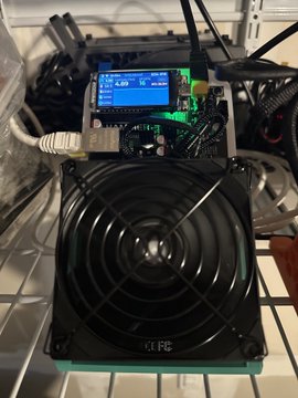 A custom-built cryptocurrency mining rig labeled 'KLFC' is shown, featuring a cooling fan and a small LCD screen displaying mining statistics.