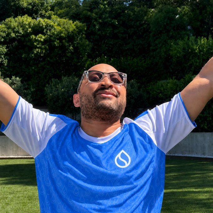 "Gm Sui guys" is a popular social media account that focuses on fitness, health, and nutrition. In the image, there's an older man wearing a blue shirt with white lettering, who appears to be enjoying his time outdoors in a park or garden setting. The photo captures him raising his arms up in the air, possibly celebrating something related to his fitness journey or simply enjoying the beautiful day outside.