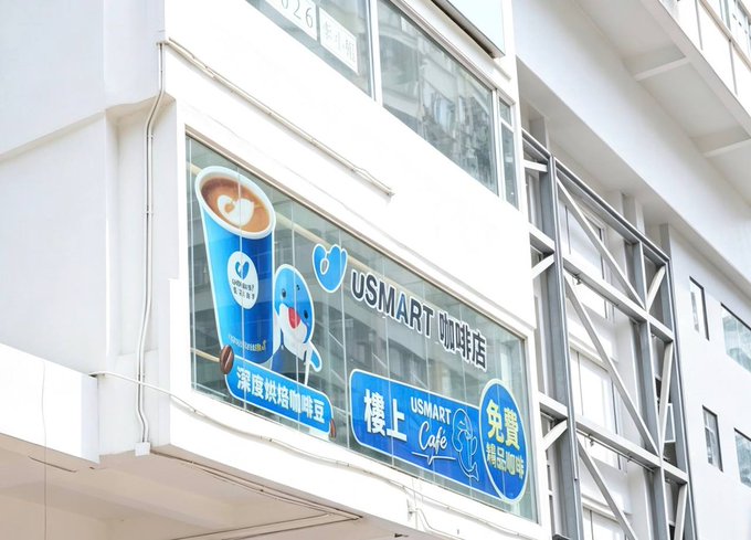 An exterior view of a building window displaying an advertisement for "USMART 咖啡店" (USMART Cafe) featuring a blue whale mascot and a cup of latte art.