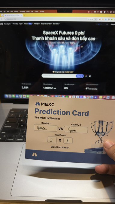 The image shows a person holding a paper ticket or card that says "World Cup Winners" on it, indicating that they have won tickets for an event. The person is standing next to a laptop computer with a monitor displaying a webpage about the World Cup.