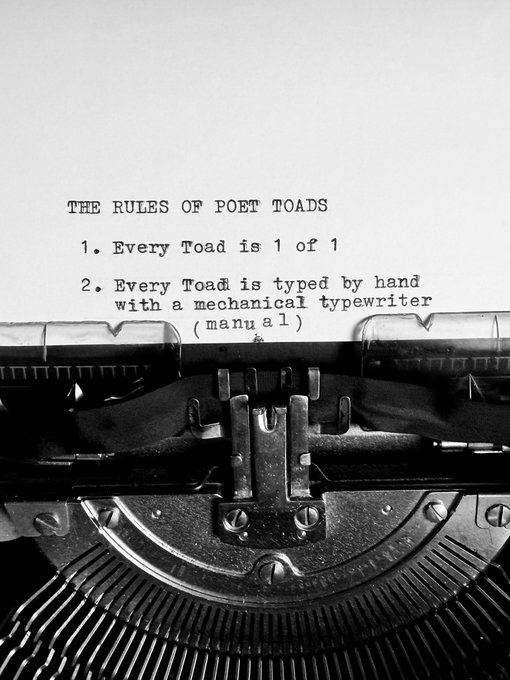 A black-and-white image of a vintage typewriter with a piece of paper loaded in it, displaying the typed text "THE RULES OF POET TOADS: 1. Every Toad is 1 of 1; 2. Every Toad is typed by hand with a mechanical typewriter (manual)."