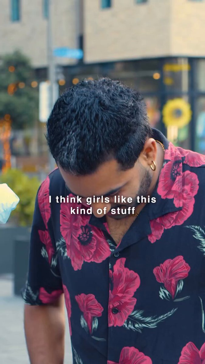 The image features a man wearing a floral shirt, with his head down as he walks past a building. The text in the image reads "I think girls like this kind of stuff", which seems to be a reference to the popular song "Bad Guy" by Billie Eilish. This reference is likely meant to convey that the man finds certain aspects of the song appealing or relatable, and he might have an interest in the artist or her music style.