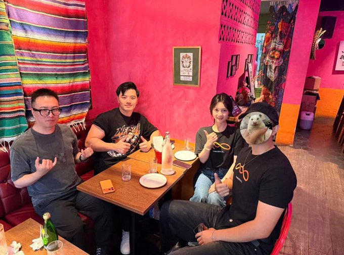 Four people sit at a wooden table in a vibrant pink-walled restaurant decorated with a colorful striped serape blanket and a tiger poster.