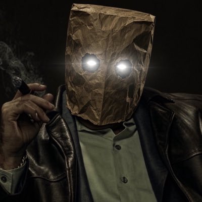 A menacing figure wearing a crumpled brown paper bag over his head with glowing white eyes peers from the shadows while smoking a cigar, perfectly capturing the post's message about staying anonymous and keeping the bag on in dangerous times.