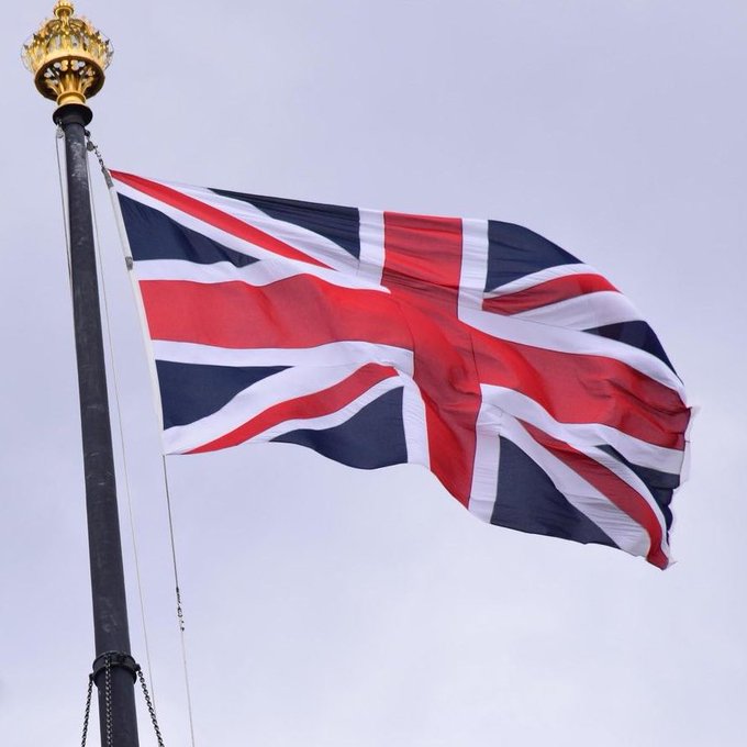 The United Kingdom flag waves against a gray backdrop, symbolizing the UK Parliament where the House of Lords recently passed an amendment requiring the government to develop a national cryptocurrency strategy.