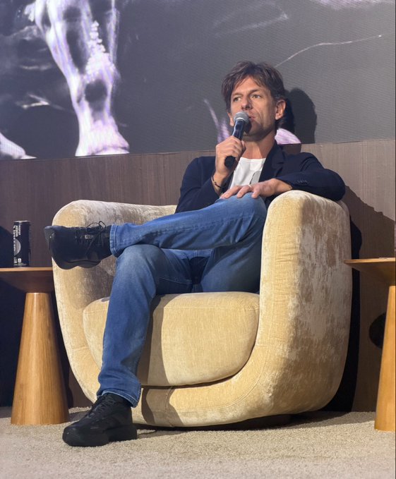 A man sits casually in a tan armchair holding a microphone, with a beverage can visible on a side table beside him. The image accompanies a post about Francesco Abbate, CEO of FIFA Collect, announcing their platform has surpassed 1 million users and discussing their decision to adopt Avalanche blockchain technology to meet their specific requirements.