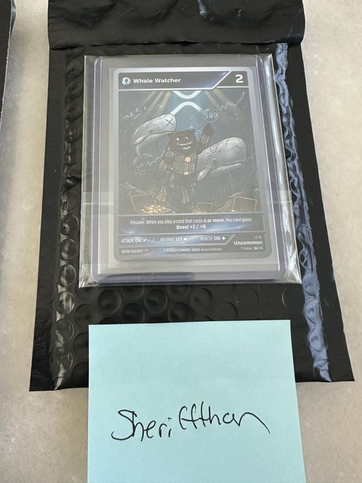 A trading card labeled 'Whale Watcher' featuring a cartoon whale character in diving gear, placed on black bubble wrap above a light blue note that reads 'Sherif Khan'.
