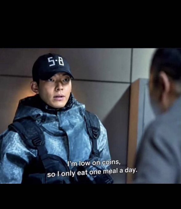 A Korean drama screenshot showing a young man in a cap marked '5-8' and tactical gear, with subtitles reading 'I'm low on coins, so I only eat one meal a day.'