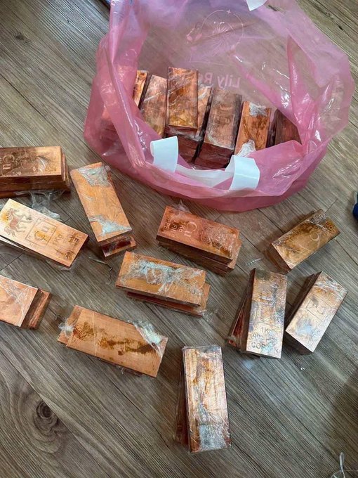 A pink plastic bag on a wooden floor containing multiple small copper bars wrapped in clear plastic packaging.