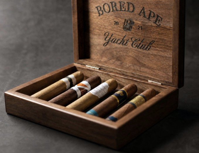 A wooden cigar box branded with 'BORED APE YACHT CLUB 2021' on the inside lid, containing several cigars with decorative bands.