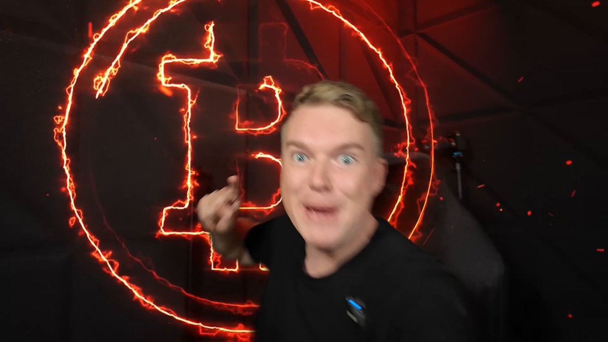 The image features a man with blonde hair wearing a black shirt, standing against a dark background that includes neon lights and a large Bitcoin logo. The man appears to be making a funny face or gesture as he looks at the camera. The text on the image reads "BITCOIN OPEN INTEREST TRAP!! WATCH BEFORE MONDAY MARKET OPEN!!! HORMUZ CLOSED AGAIN!! WATCH NOW youtu.be/0KpSXi-uxUs". This suggests that there is a Bitcoin-related event or promotion happening, and the man's reaction could be related to this.