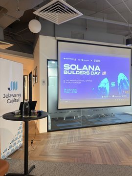 A presentation screen displays "SOLANA BUILDERS DAY" with event details including "1 NOV '23, 9AM-6PM," set up in a co-working space featuring a Jelawang Capital banner nearby, promoting the upcoming event co-hosted by SuperteamMY, Solana Spaces, and Superscrypt.